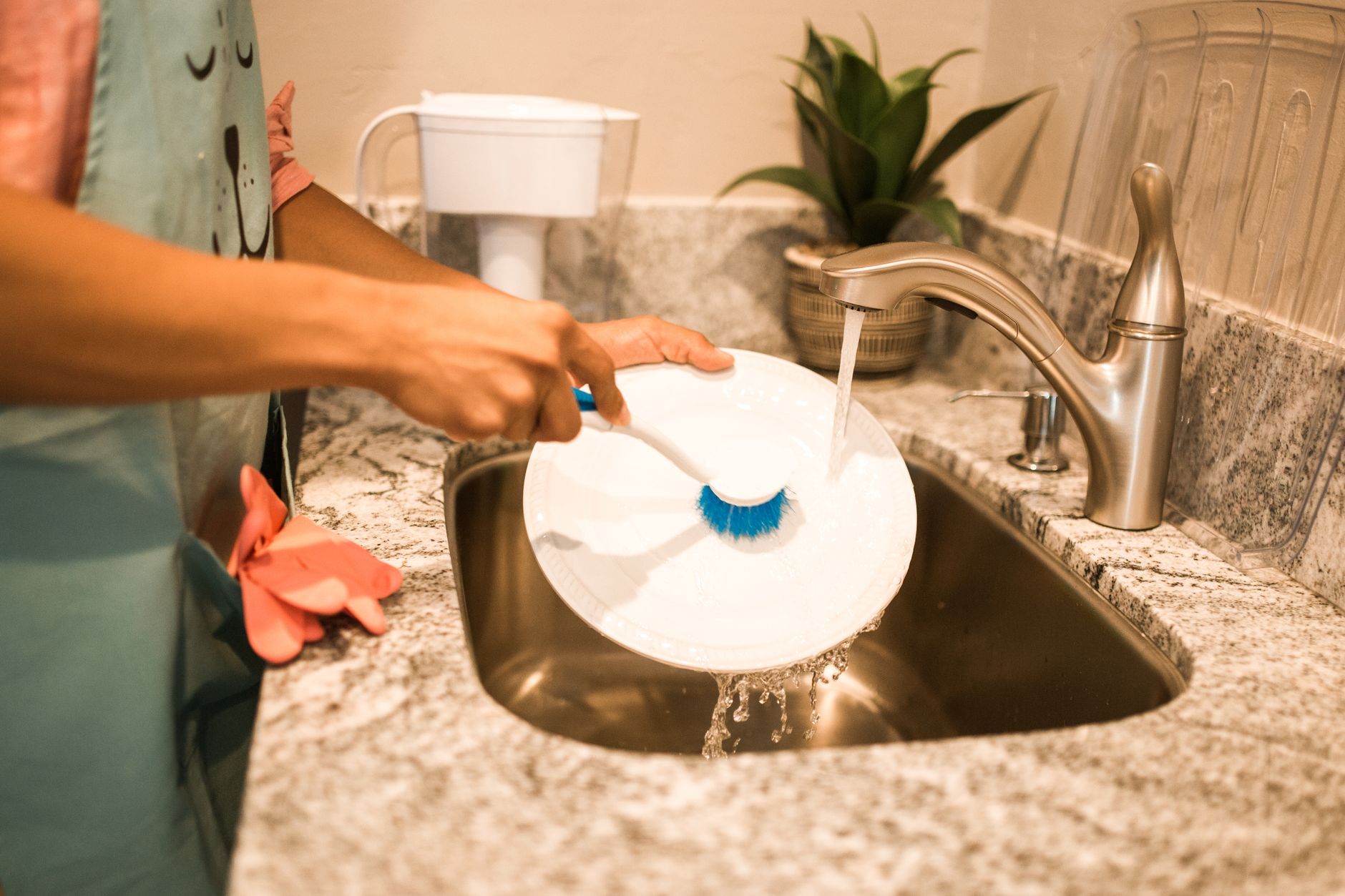 Personne qui frotte une assiette sous l'eau du robinet